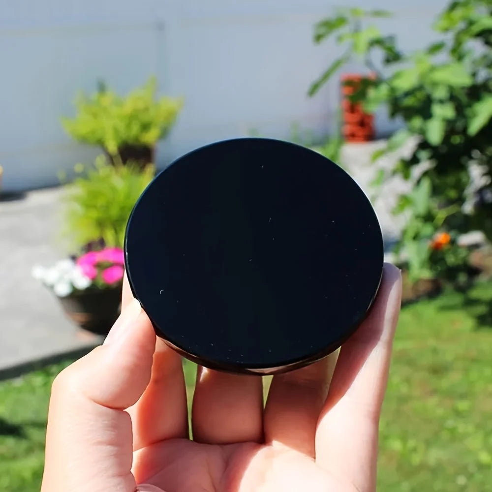 A hand holds a round, black obsidian mirror for Feng Shui and divination outdoors.