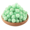 A pile of light green textured resin beads for jewelry making in a wooden bowl.
