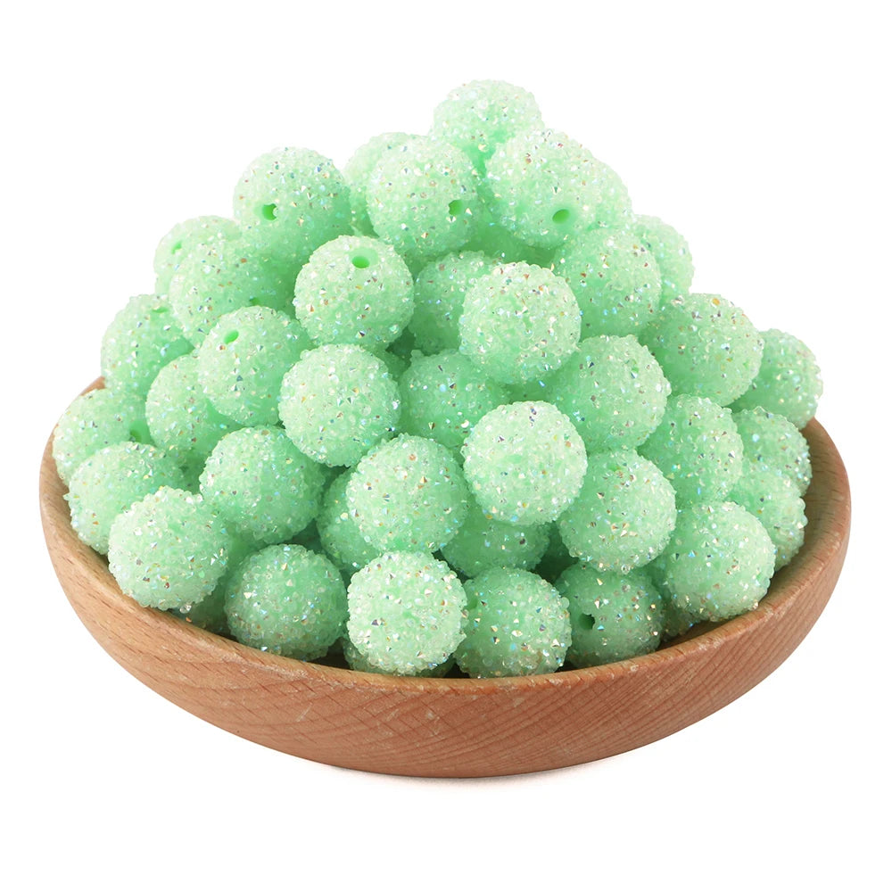 A pile of light green textured resin beads for jewelry making in a wooden bowl.