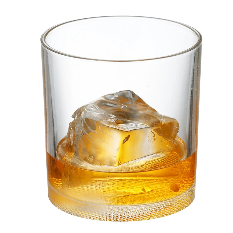 A heavy base tumbler glass filled with amber whiskey and a large ice cube.