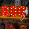Letrero de luz LED naranja 3D que deletrea 'BOO' sobre una estantería de madera con un atrezo de esqueleto.