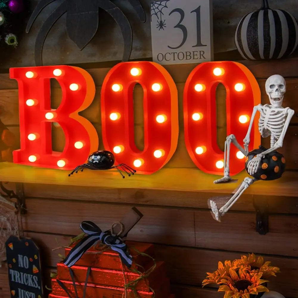 Letrero de luz LED naranja 3D que deletrea 'BOO' sobre una estantería de madera con un atrezo de esqueleto.