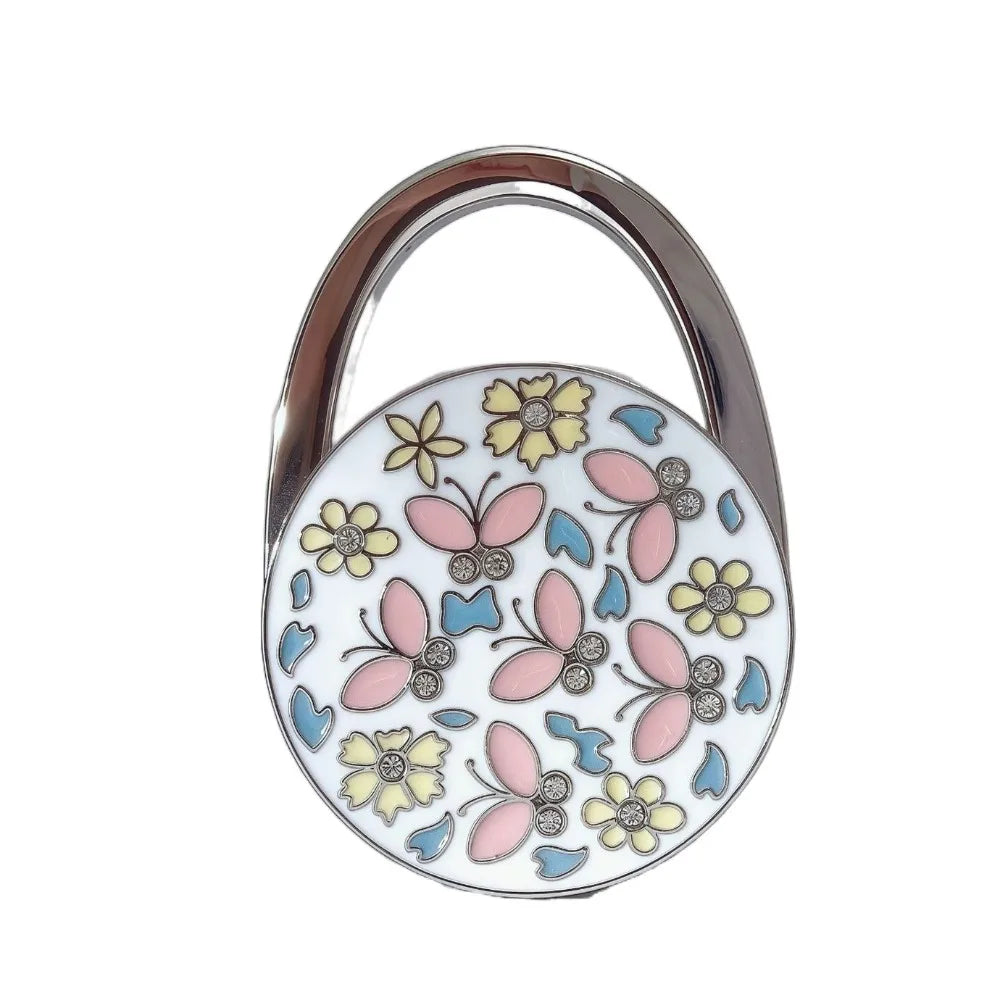 A silver handbag hook with a floral crystal design featuring pink and yellow butterflies.