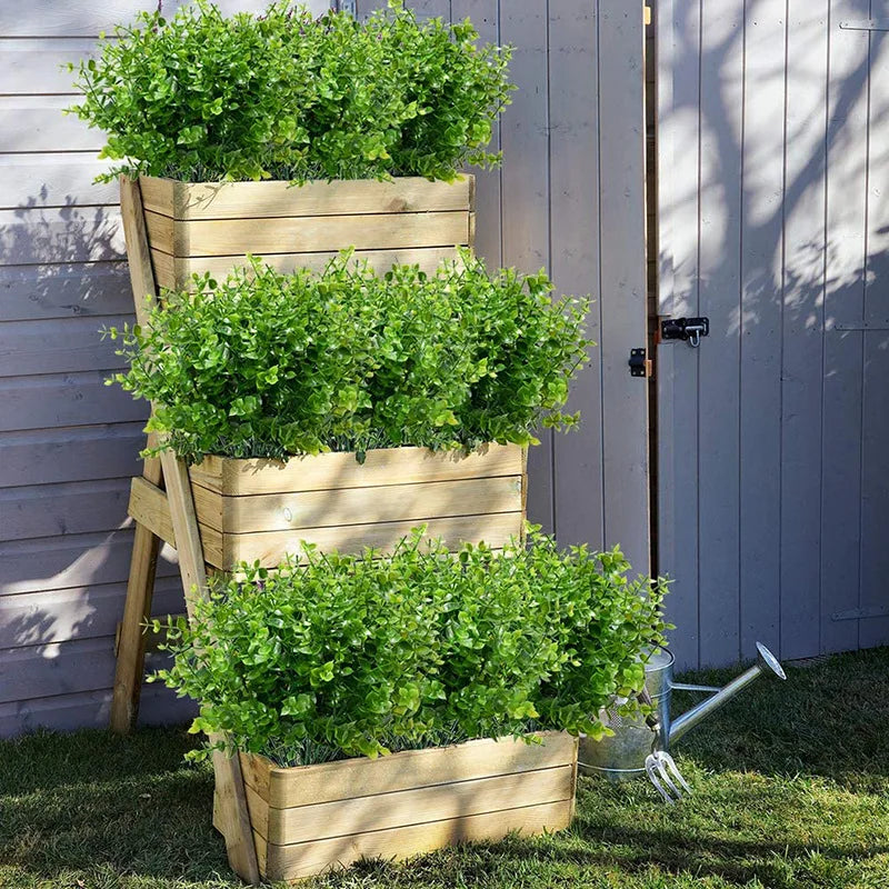 Trois jardinières en bois remplies de feuilles d'eucalyptus artificielles vert vif, devant un mur gris clair.