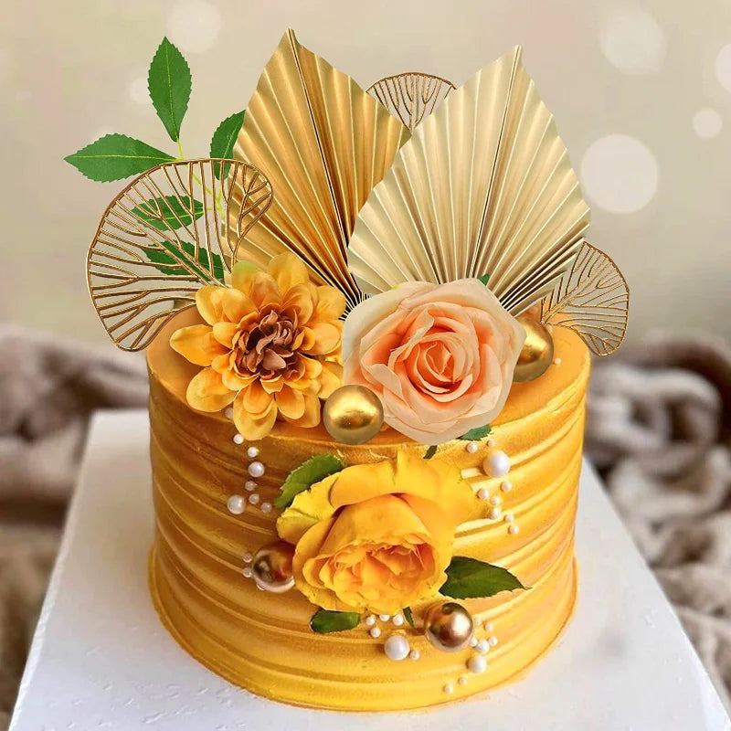 A golden cake decorated with orange and peach roses and palm leaf accents.
