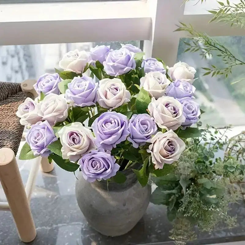 A bouquet of purple and white artificial roses in a gray vase on a glass table.