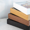 A stack of three wooden shadow boxes with varying wood tones and a white frame displaying dried flowers.