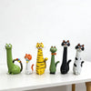 A collection of seven cat-shaped resin figurines in various colors and poses displayed on a white surface.