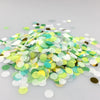 A pile of multicolor paper confetti consisting of green, yellow, and white pieces scattered on a light surface.