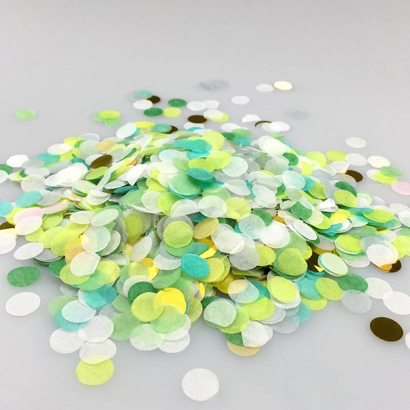 A pile of multicolor paper confetti consisting of green, yellow, and white pieces scattered on a light surface.