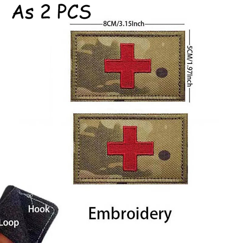 Two embroidered tactical morale patches featuring a red cross on olive drab fabric with a hook and loop.
