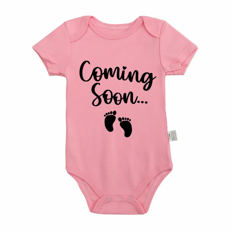 Pink baby bodysuit with black text that reads Coming Soon