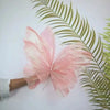 Pink silk artificial butterfly decoration resting on a green palm leaf.