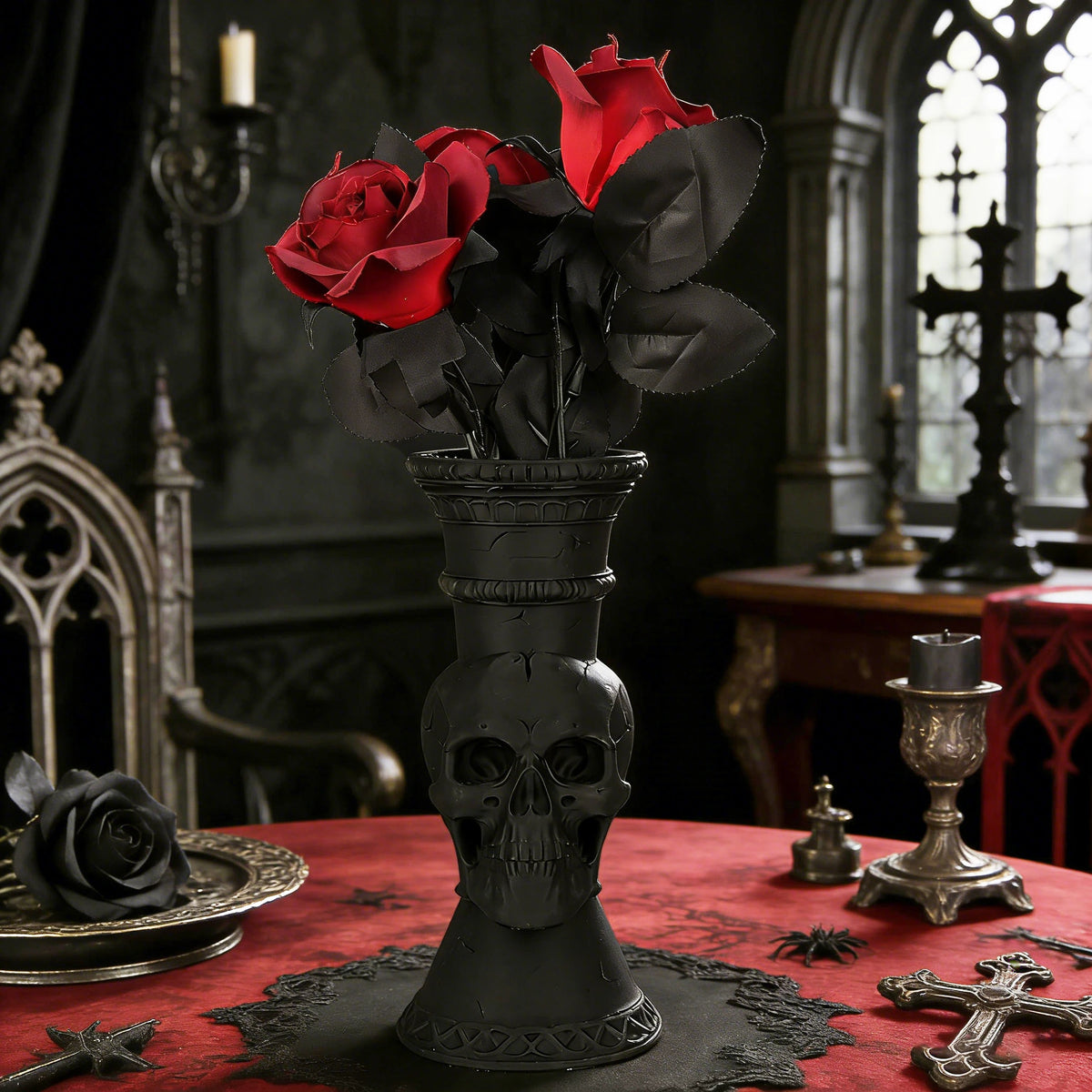 A dark gothic decorative vase shaped like a skull holding red roses on a red table.
