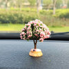 A small tree ornament with pink flowers sits on a black car dashboard.