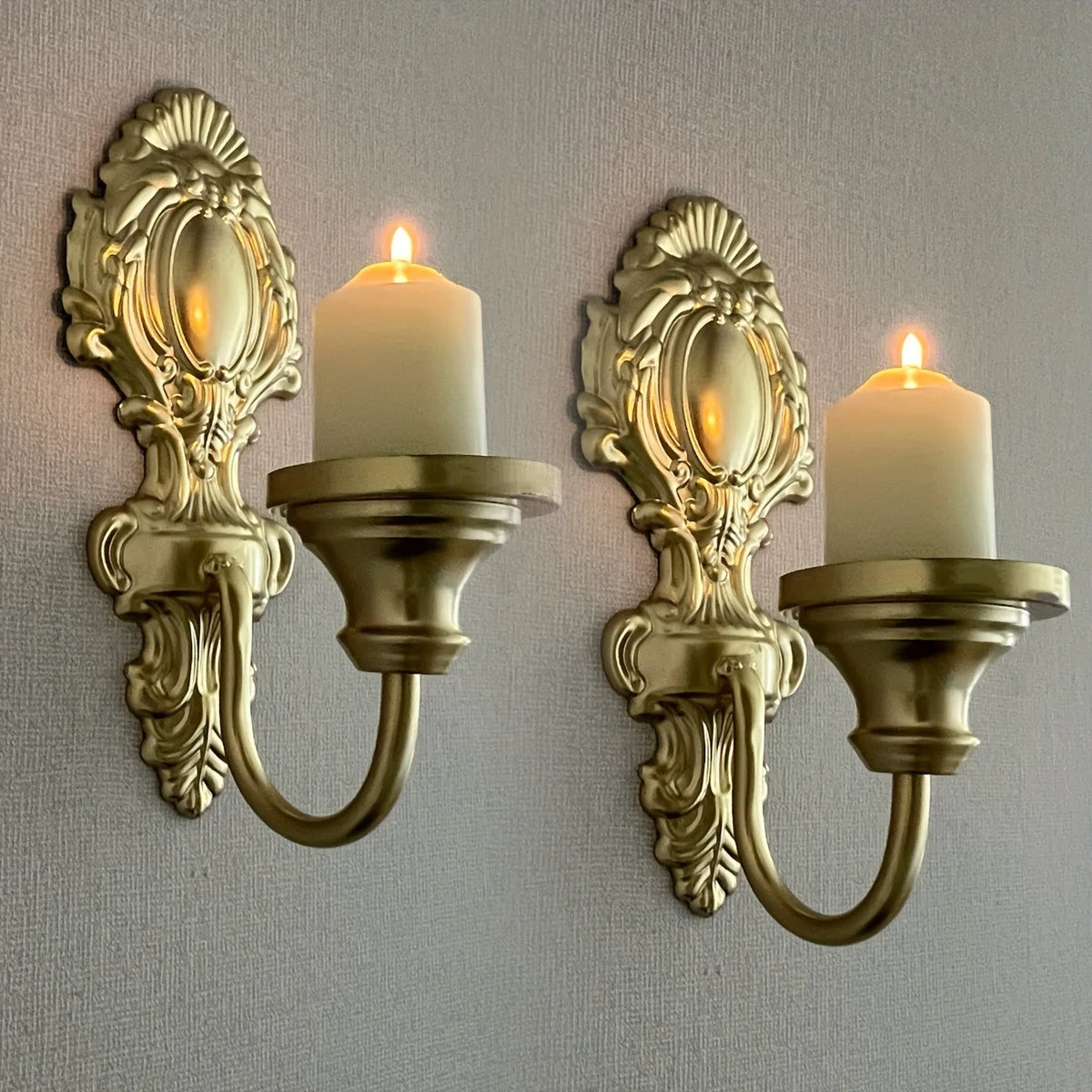 A set of two vintage wrought iron wall-mounted candle holders with white pillar candles.