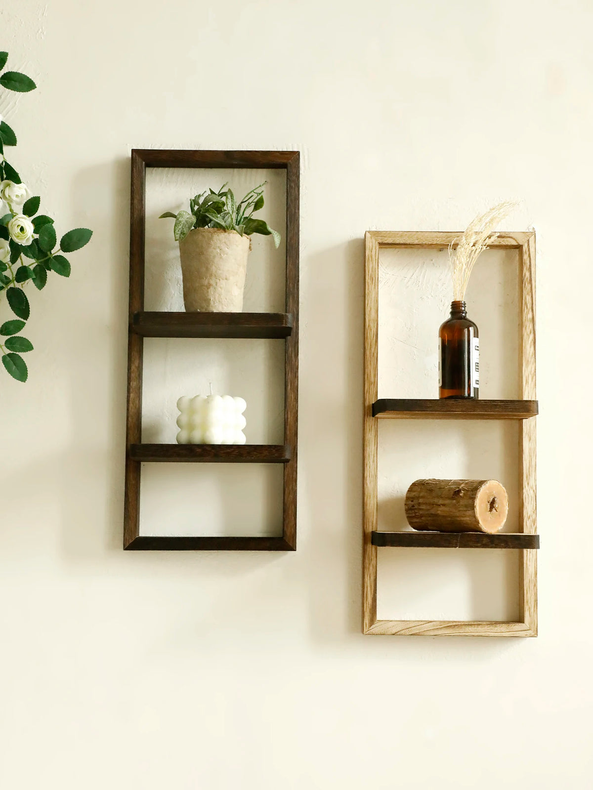 A rustic wooden floating shelf with two tiers displaying a potted plant and a white candle.