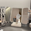A triple fold LED makeup mirror with storage tray and multiple mirrors shown on a gray surface.