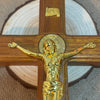 A wooden crucifix with a gold-colored Jesus figure mounted on a cross, set against a light background.