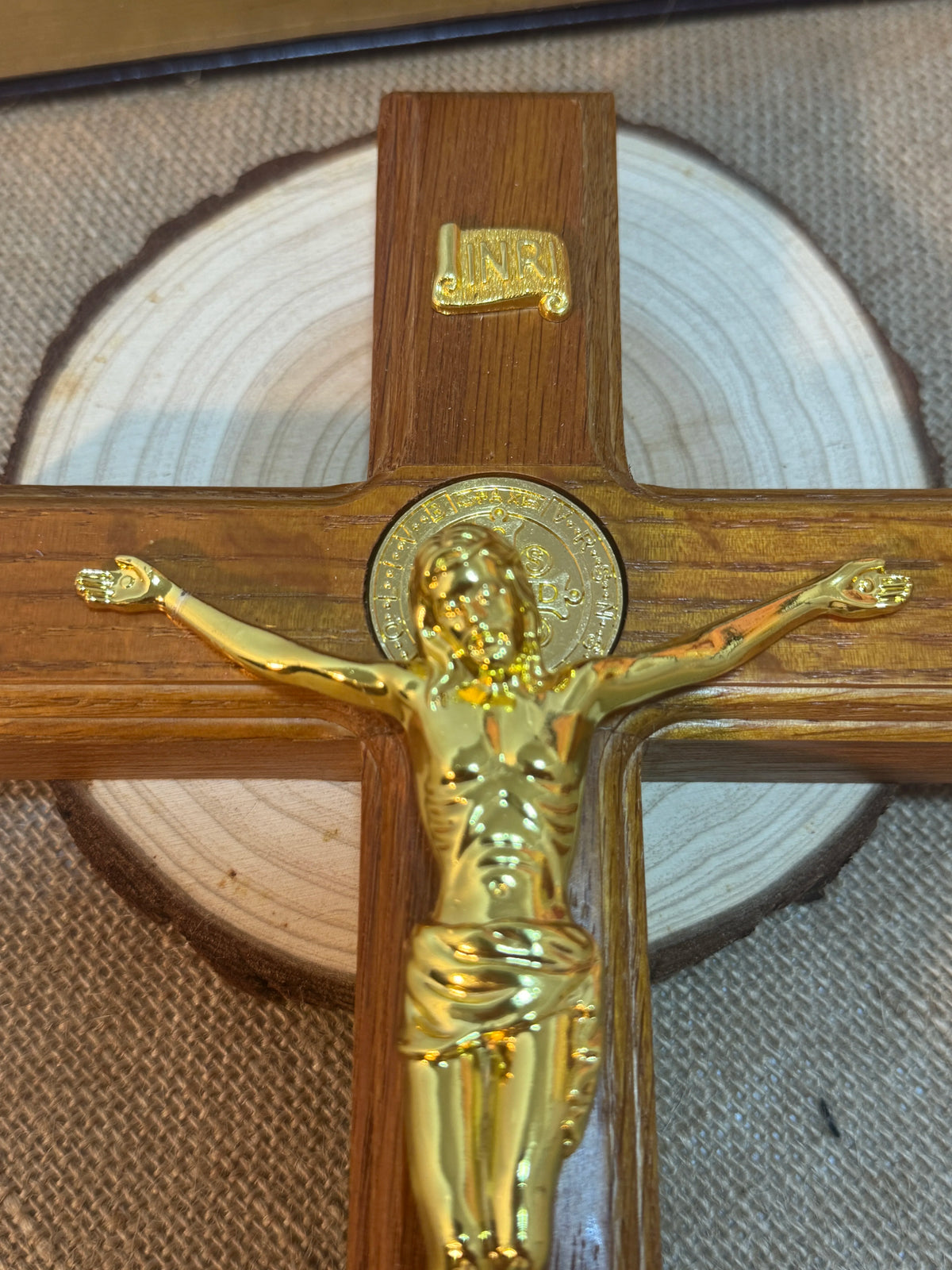 A wooden crucifix with a gold-colored Jesus figure mounted on a cross, set against a light background.