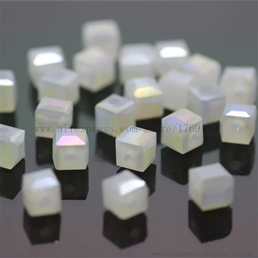 A collection of square cut glass crystal beads in white and clear colors displayed on a dark surface.