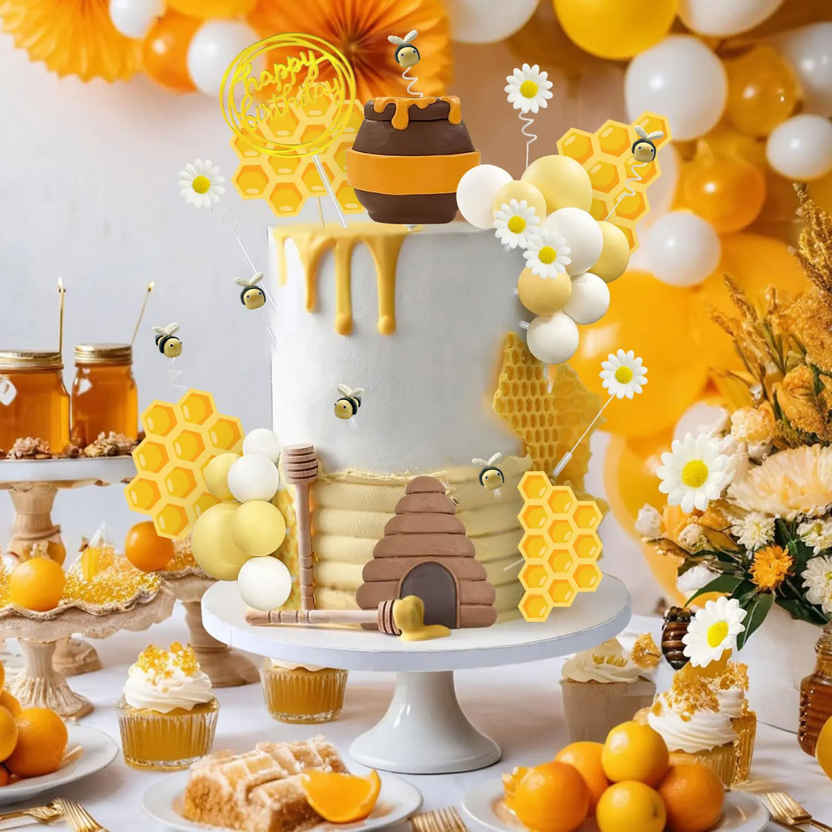 A tiered cake decorated with yellow and white elements, including bee-themed toppers, honeycomb shapes, and honey jars.