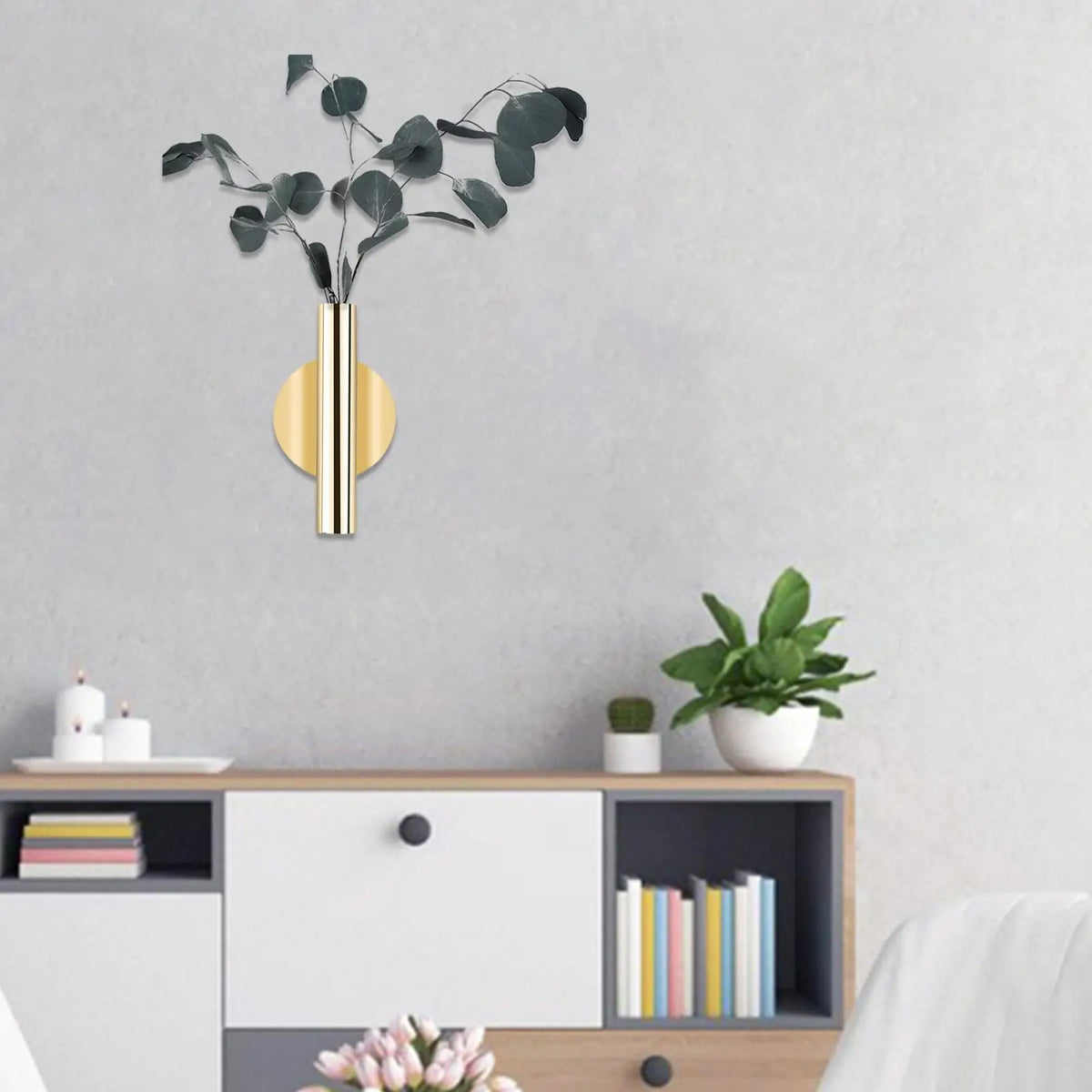 A modern wall-mounted flower vase with an elegant gold finish displaying dark green eucalyptus branches.