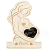 A light wood sign featuring a silhouette of a woman holding a dark heart, symbolizing love and motherhood.