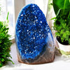 A deep blue, rough crystal cluster decor resting on a white surface next to green foliage.