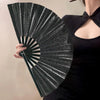 A hand fan with a glitter holographic design is held open, showing radiating lines against a dark background.
