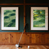 A canvas print featuring a green golf course landscape with small figures, displayed on a dark green wall above wooden paneli
