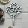 A silver acrylic birthday cake topper with the words Happy Birthday on a stick, placed next to a slice of citrus fruit.