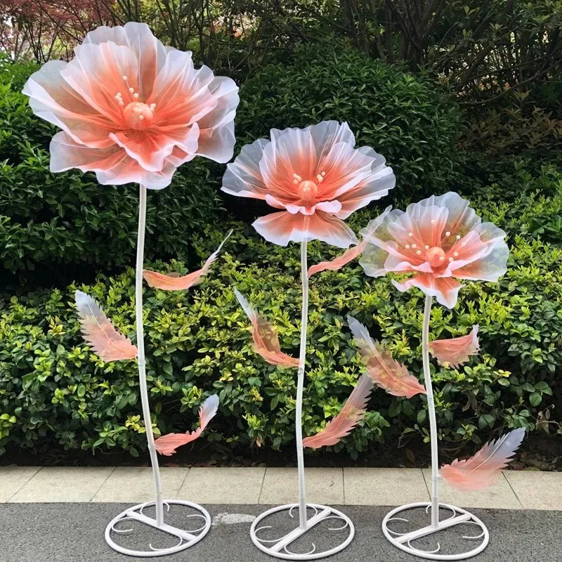 A set of three large, delicate pink and white velvet mesh flowers on metal stands.