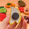 A hand holds a yellow and white fruit magnet next to various colorful fruit magnets.
