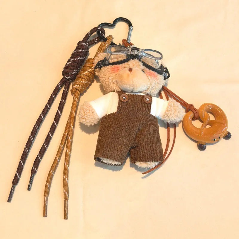 Un ours en peluche portant des lunettes aviateur et une tenue marron, attaché à une chaîne en cuir.