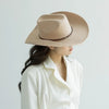 A woman wearing a beige classic wool cowboy hat with a studded leather band and a white collared shirt.