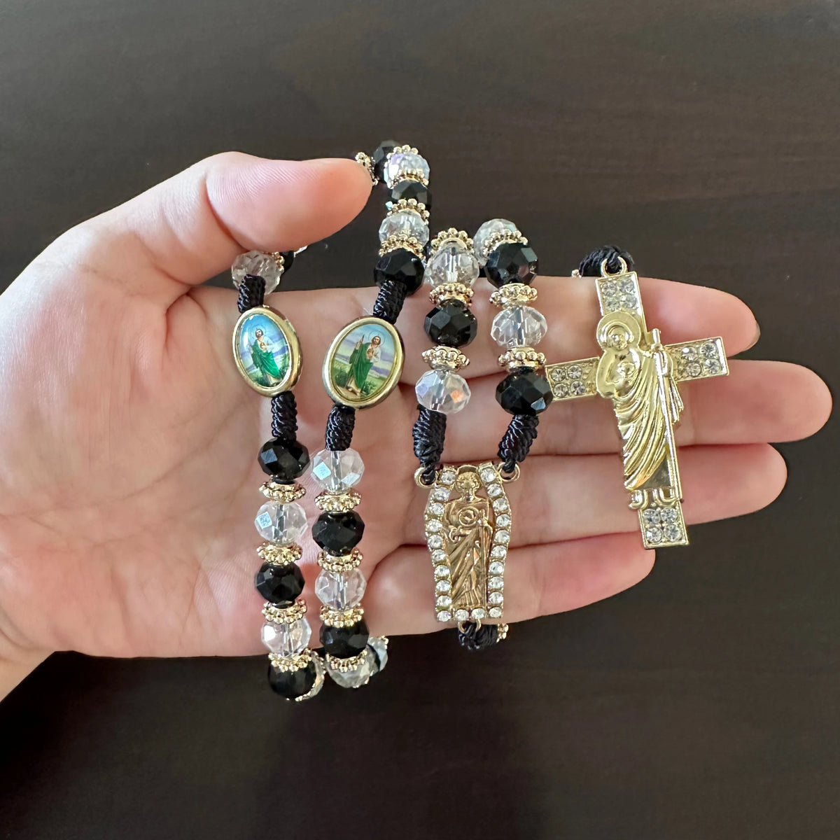A hand holds a green crystal rosary necklace featuring Saint Jude and Virgin Mary cross pendants.