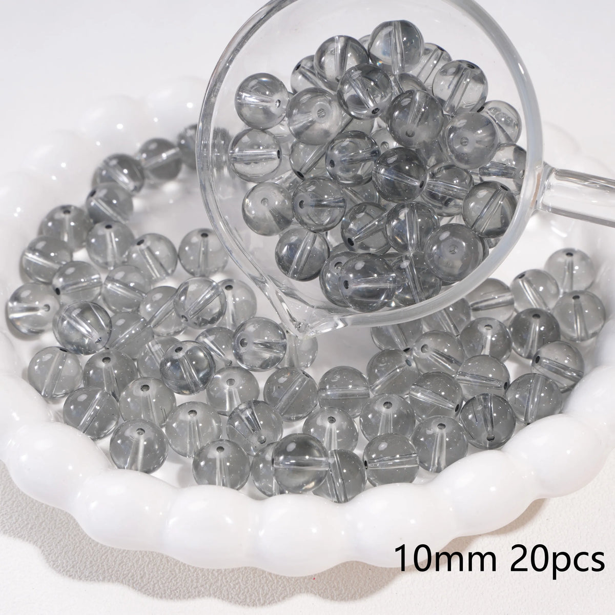 A clear glass spacer bead is shown in a small glass container with many beads spilled around it.