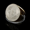 Una moneda metálica de oro conmemorativa que presenta el símbolo de Bitcoin sobre una superficie transparente.