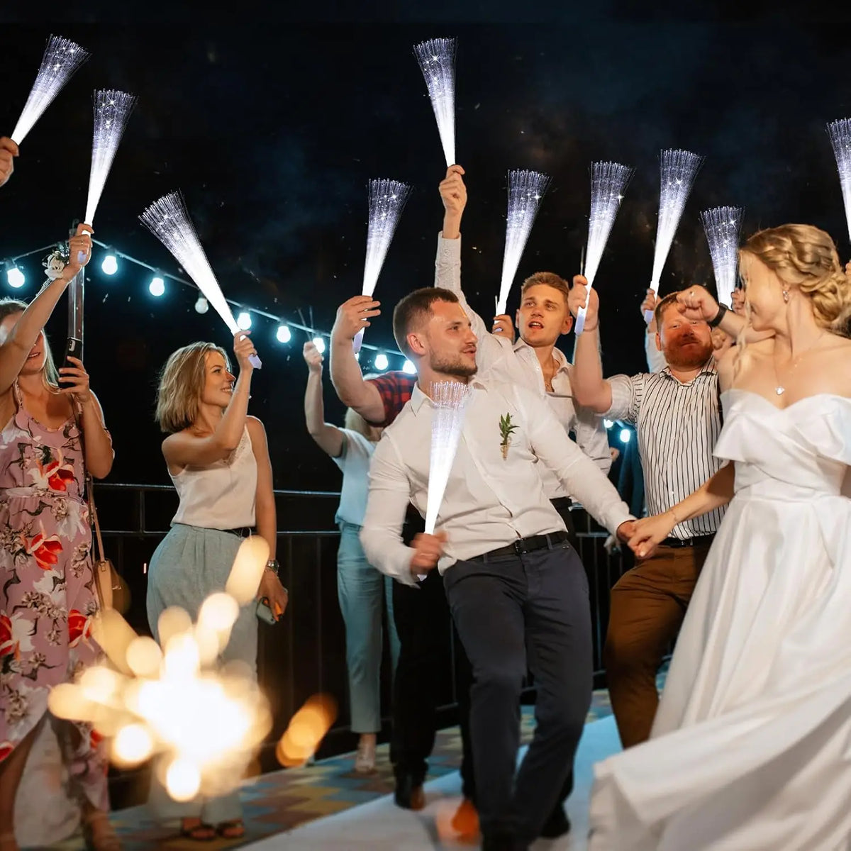 A group of people are holding LED fiber optic glow wands in a performance or celebratory setting.