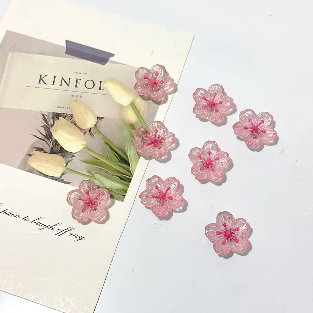 Pink cherry blossom fridge magnets arranged on a white background with a light-colored card.