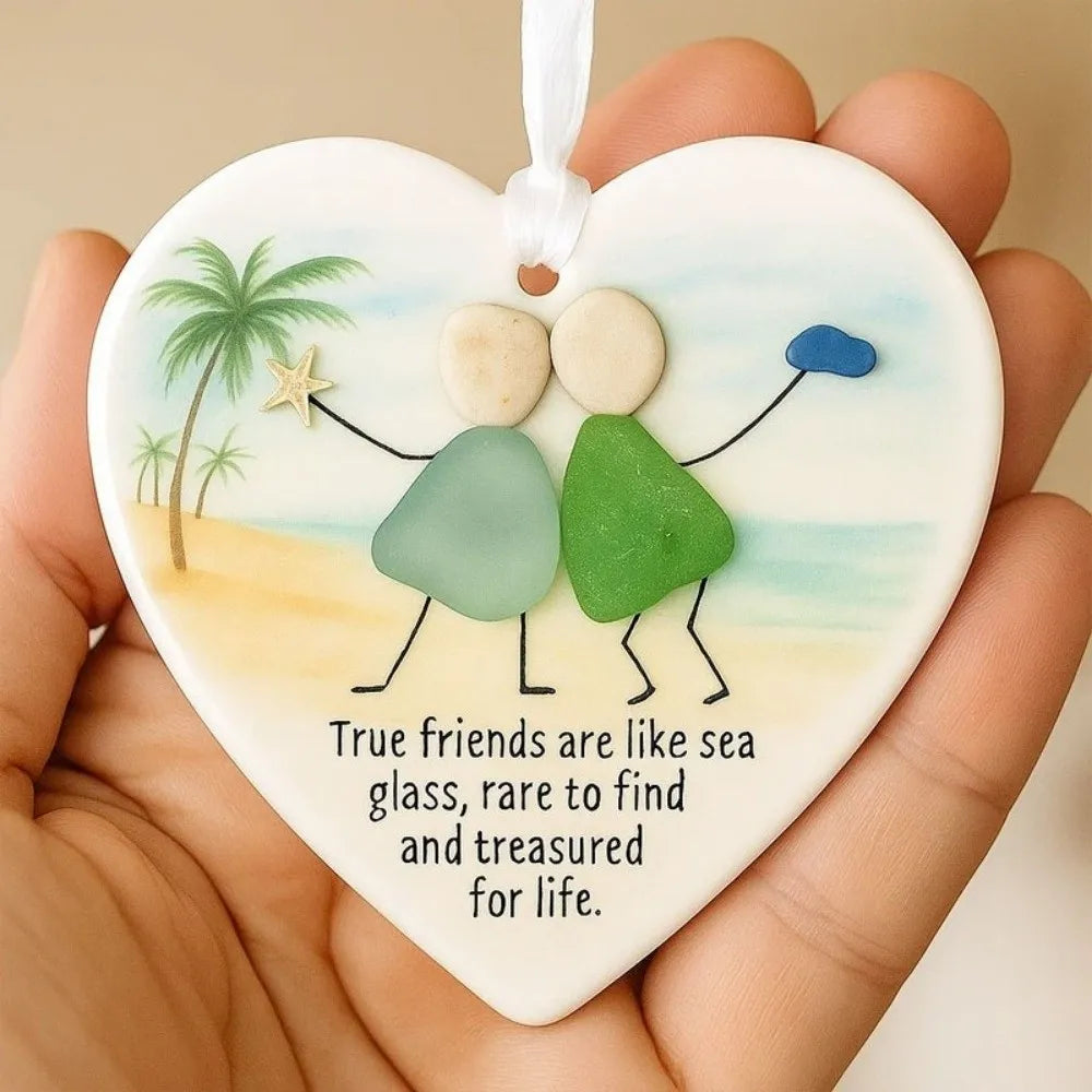 A heart-shaped acrylic pendant featuring sea glass elements and a palm tree design, held in a hand.