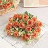 A bouquet of five silk touch artificial orange roses with green foliage arranged on a white surface.