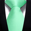 A bright mint green silk necktie tied in a simple knot against a black suit jacket.