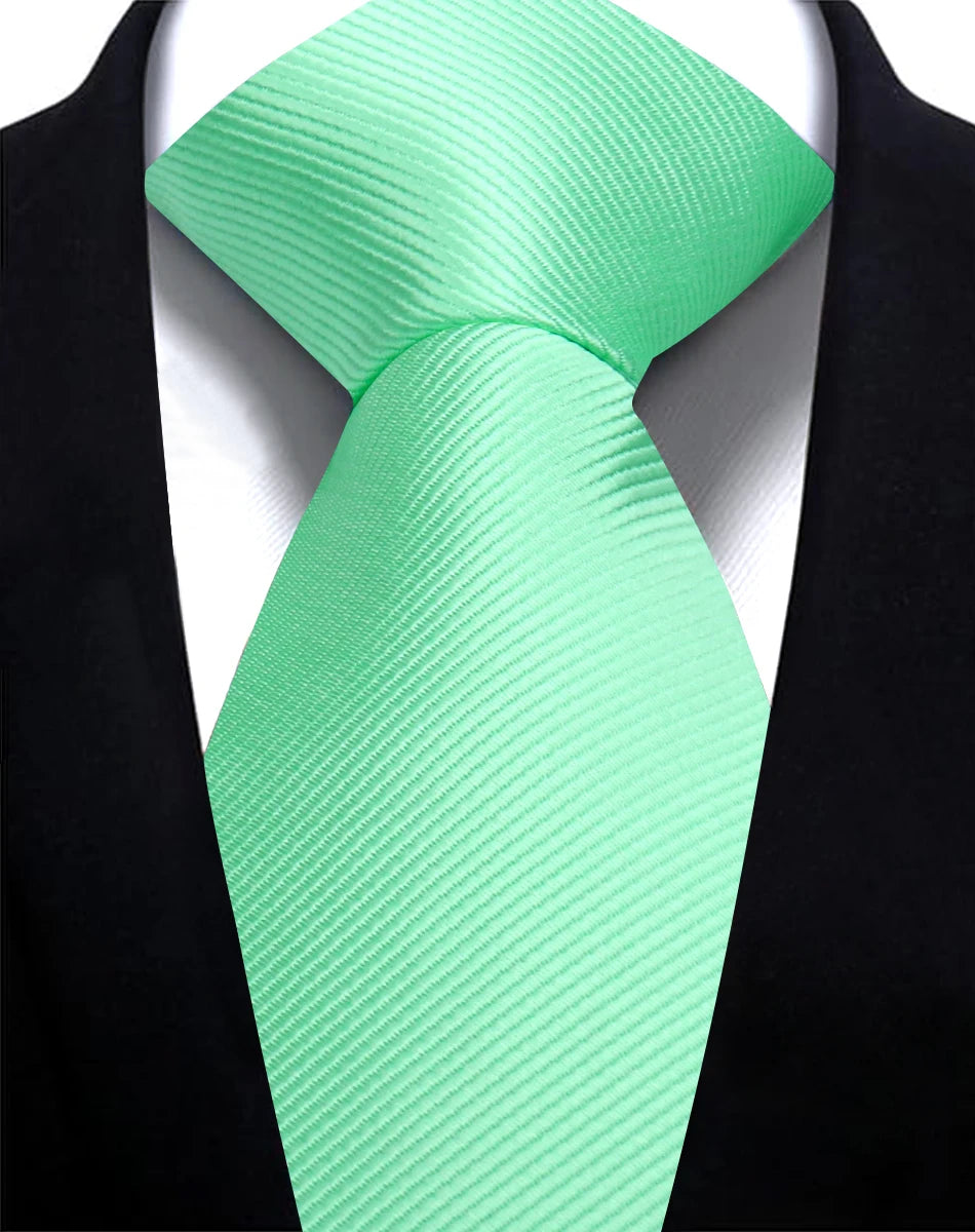 A bright mint green silk necktie tied in a simple knot against a black suit jacket.