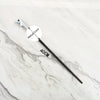 A black metal magic wand replica with a silver handle and a labeled metal core on a white marble surface.