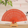 Hand carved bamboo folding fan in orange color displayed on a wooden stand.