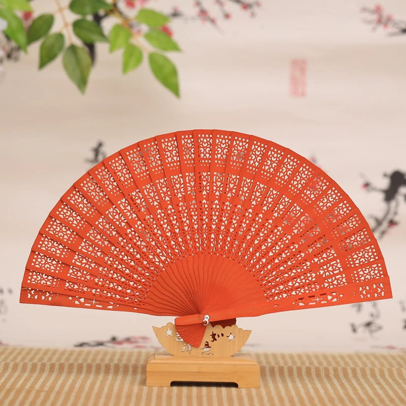 Hand carved bamboo folding fan in orange color displayed on a wooden stand.