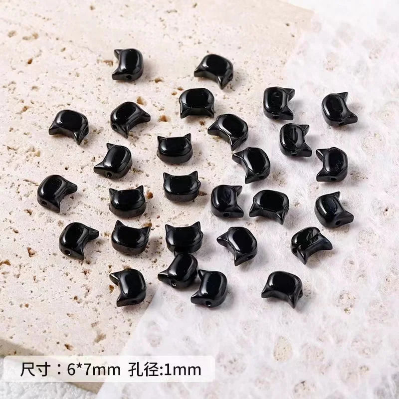 A collection of small black cat head glass beads for jewelry making, displayed on a white surface.