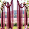A sheer burgundy tulle backdrop with draped fabric and floral accents for an elegant event or celebration.